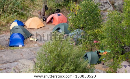 Camping tents placed on a stony area surrounded by wild vegetation at the mountains