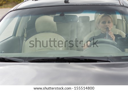View through the front windscreen of a female driver drinking alcohol from a bottle in the car while driving along the road