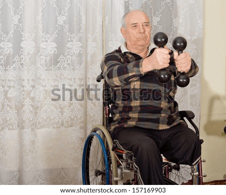 Senior handicapped man exercising with a pair of dumbbells to strengthen his arms while sitting in a wheelchair