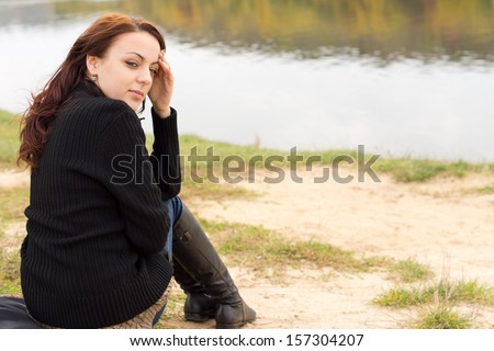 Beautiful woman enjoying the tranquillity of the outdoors sitting above calm water with autumn reflections looking back over her shoulder at the camera