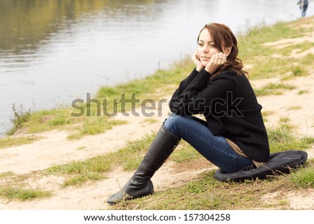 Beautiful trendy young woman sitting on a cushion on a river bank enjoying nature as she rests her chin on her hands in contentment