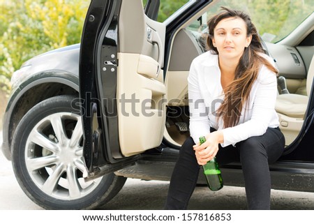 Lonely unhappy drunk woman sitting at the roadside in her parked car drinking alcohol directly from the bottle