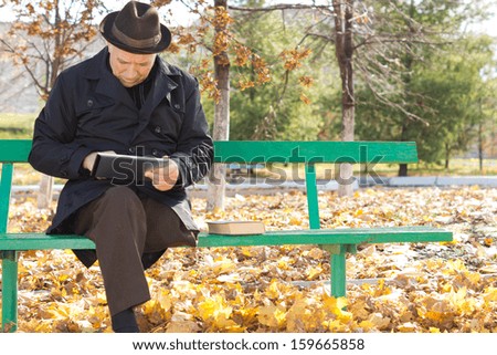 Senior one legged disabled man relaxing with a tablet computer sitting enjoying the fresh air and sunshine in an autumn park
