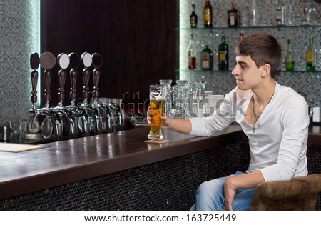 Attractive young man sitting at a counter drinking a pint of draught beer alone on a pub as he waits for his friends to arrive