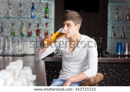 Young man alone drinking in a pub sitting at the bar counter slugging back a pint of draught beer