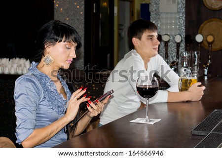 Elegant young woman with manicured red nails sitting texting on her mobile at the bar counter in a nightclub, side view