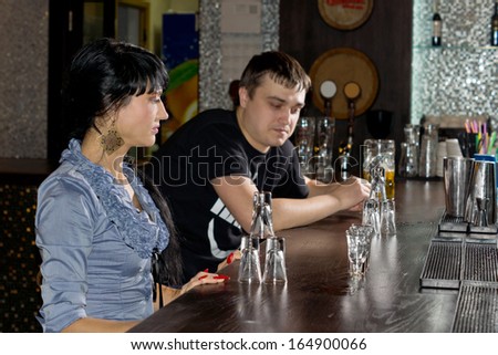 Two friends drinking vodka shots sitting at the counter in the bar eye the last full glass as they decide who will drink it