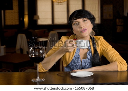 Attractive young woman sitting at a bar counter talking to the camera as she drinks a cup of hot espresso coffee