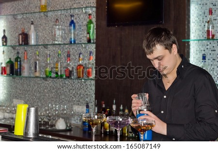 Barman in a pub preparing alcoholic cocktails standing behind the counter mixing drinks in three elegant cocktail glasses