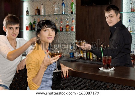 Two young friends relaxing in a pub sitting drinking glasses of red wine at a bar counter with the barman working alongside them
