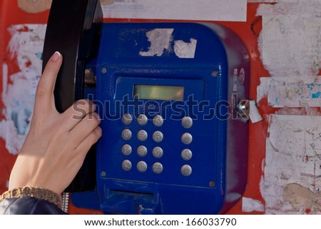 Woman using a public telephone reaching out with her hand to take the handset off the cradle