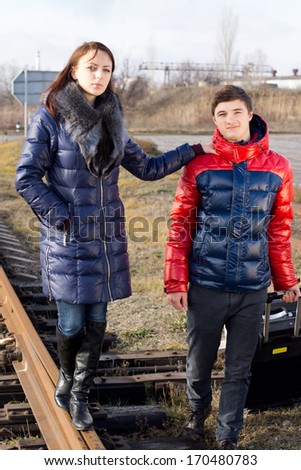 Fashionable young couple in warm winter clothing standing on a railway line with the girl holding onto her boyfriends shoulder as she balances on the track