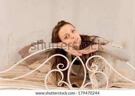 Beautiful young woman sitting daydreaming with her arms and chin resting on a curved wrought iron rail at the foot of as bed