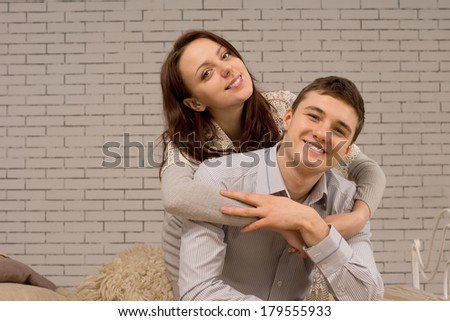 Happy attractive young couple relaxing together hugging each other as they sit together indoors in front of a painted brick wall with copyspace