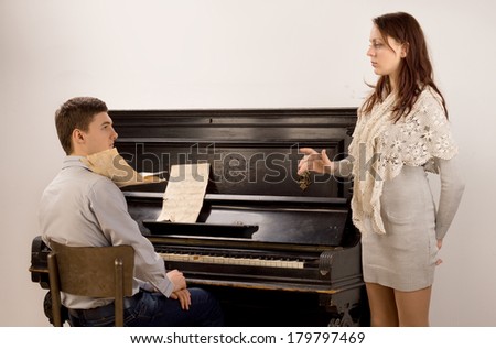 Young couple practicing a classical duet pausing for a discussion as the pretty female vocalist raises an issue with the young male pianist
