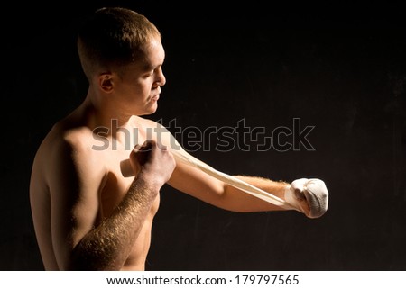 Dark dramatic image of a barechested young boxer putting on his bandages before a fight with a look of concentration