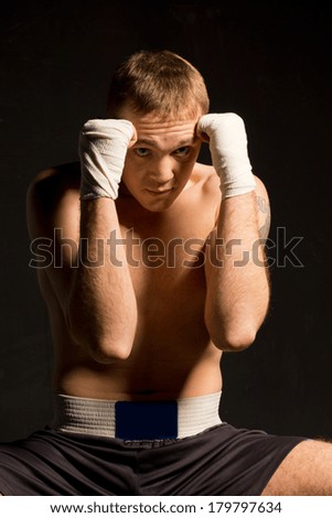 Young boxer protecting his head by raising both his bandaged fists in a defensive position against a dark background