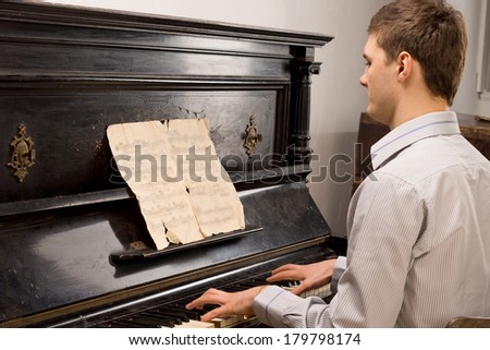Young man playing music on a retro upright wooden piano as he practices the classics for a recital or performance