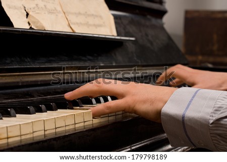 Male pianist practicing sitting at an upright piano playing music from an old score sheet, close up of his hands