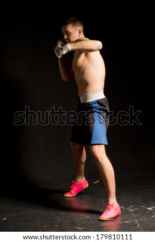 Fit strong young boxer working out in the ring in the darkness standing ready to throw a punch at the camera, full length portrait