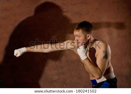 Young boxer punching an opponent during a fight in the ring with his fist extended and the shadow of his opponent cast on the wall behind him