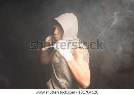 Young boxer about to throw a punch turned at an angle to the camera with his arm drawn back about to launch himself forwards in a dark smoky environment