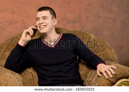 Happy young man chatting on his mobile phone laughing with pleasure as he listens to the conversation while relaxing in an armchair