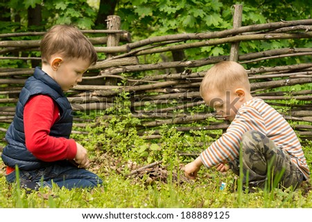 Two young boys playing at lighting a campfire kneeling down together carefully applying a lit match to a pile of twigs and wood that they have gathered at a rustic campsite