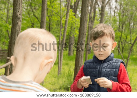 Serious little boy standing lighting a match as he plays with a young friend in rural woodland
