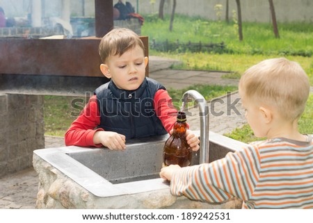 Two young boys filling a bottle of water from a running tap over a stone sink at a campsite