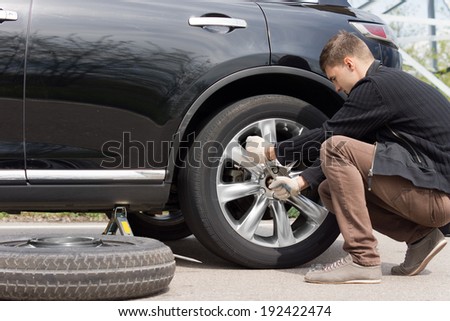 Man changing his spare wheel replacing the original tyre with a fixed puncture tightening the nuts with a wheel spanner