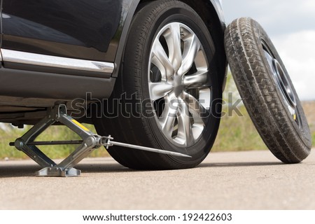 Jacking up a car to change a tyre after a roadside puncture with the hydraulic jack inserted under the bodywork raising the vehicle and the spare wheel balanced on the side
