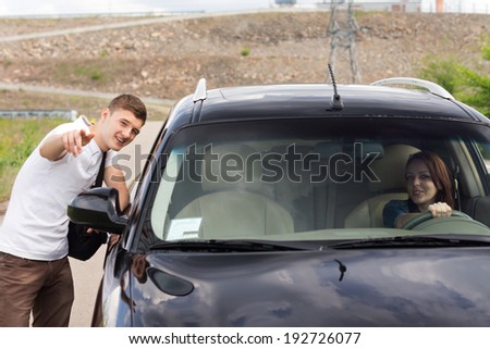 Young man giving directions to a woman driver standing talking to her through the passenger window and pointing out the route with his hand