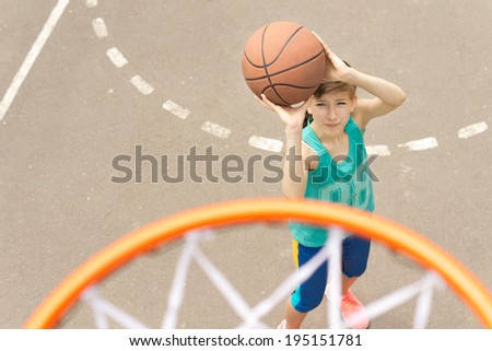 Young girl taking aim at the goal on a basketball court standing with the ball raised aiming at the hoop, view from above