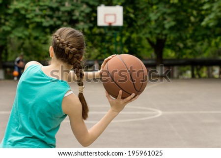 Young slender teenage girl playing basketball throwing the ball, view from behind