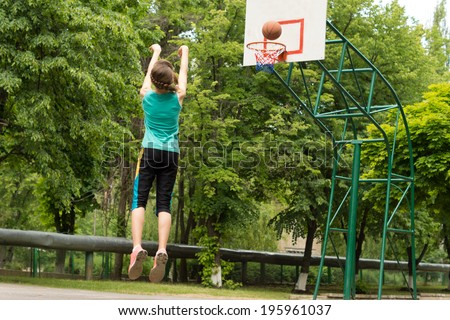 Skilled athletic young female basketball player shooting a goal on an outdoor court jumping in the air as she throws the ball, view from behind