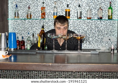 Barman keeping an eye on the cocktails he is mixing bending down low to check the liquid after adding a liqueur from a bottle
