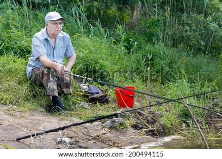 Senior handicapped man with an above knee amputation fishing on a lake shore with a rod and reel against lush greenery