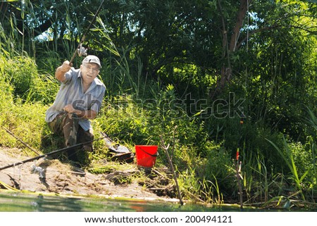 Handicapped man with a leg amputation sitting on a lake shore casting his line when fishing with his rod raised in the air