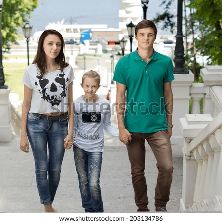 Attractive couple walking with a pretty little girl holding her hands as they all smile at the camera with ascending a flight of stairs from a river or harbour