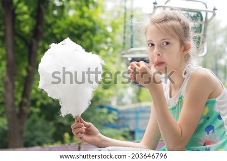 Pretty young girl eating a stick of candy floss picking at the sticky spun sugar with her fingers before placing it in her mouth with obvious pleasure