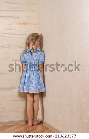Little girl being punished standing in the corner facing into the wall in her pretty blue dress and bare feet