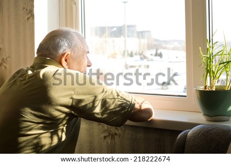 Lonely old man in an old-age home staring out of a window as he longs for his freedom and friends