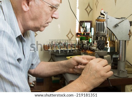Close up side profile of a senior man wearing glasses working at a workbench with small precision tools