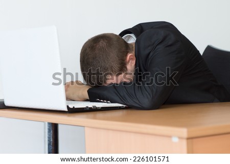 Tired Young Office Man in Black Business Suit Take a Nap on His Desk In Front His Computer.