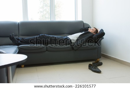 Young Handsome Office Man Lying on the Gray Couch at Lounge Area During Work Break Hours.