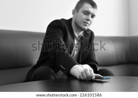 Young Good Looking Male Executive Putting His Mobile Phone on the Table at the Lounge Area. Captured in Gray Scale.