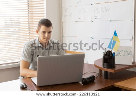 Young White Male Office Worker Busy Working with His Laptop Computer at His Table Area.