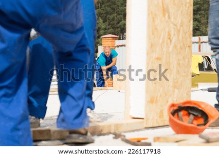 Men working on a construction site with selective focus past legs to a workman in the distant taking a measurement of the floor of the new build house