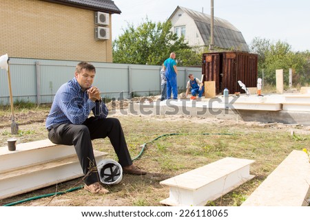 Middle Age Male Building Engineer Take a Break with Helmet on Ground. Sitting on White Bars While Thinking Something.